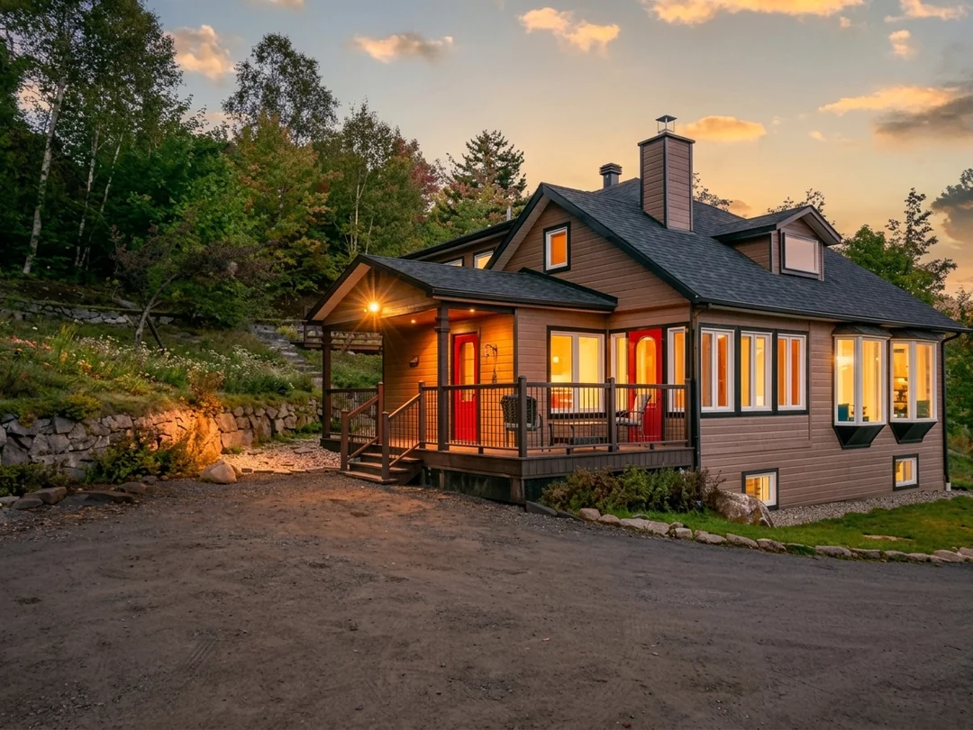 Wooden cottage lit at sunset with a covered porch and a red door