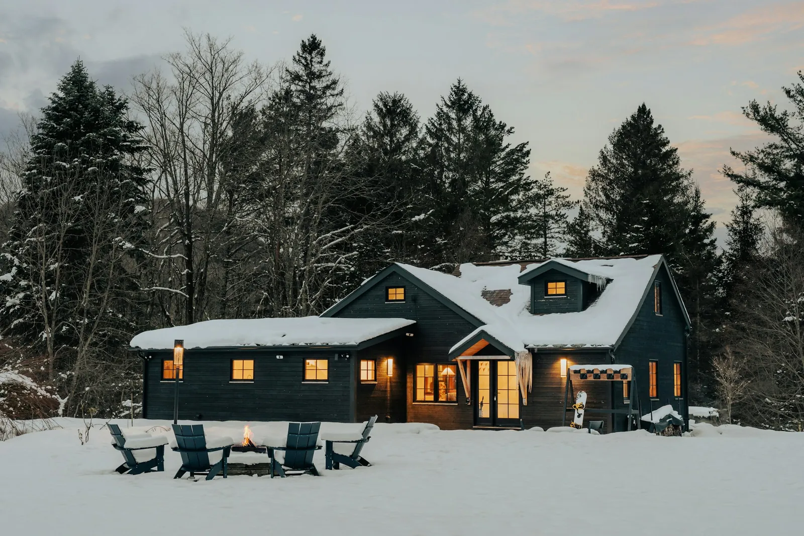 Chalet de prestige illuminé au crépuscule en hiver, avec feu extérieur, loué comme investissement locatif au Québec