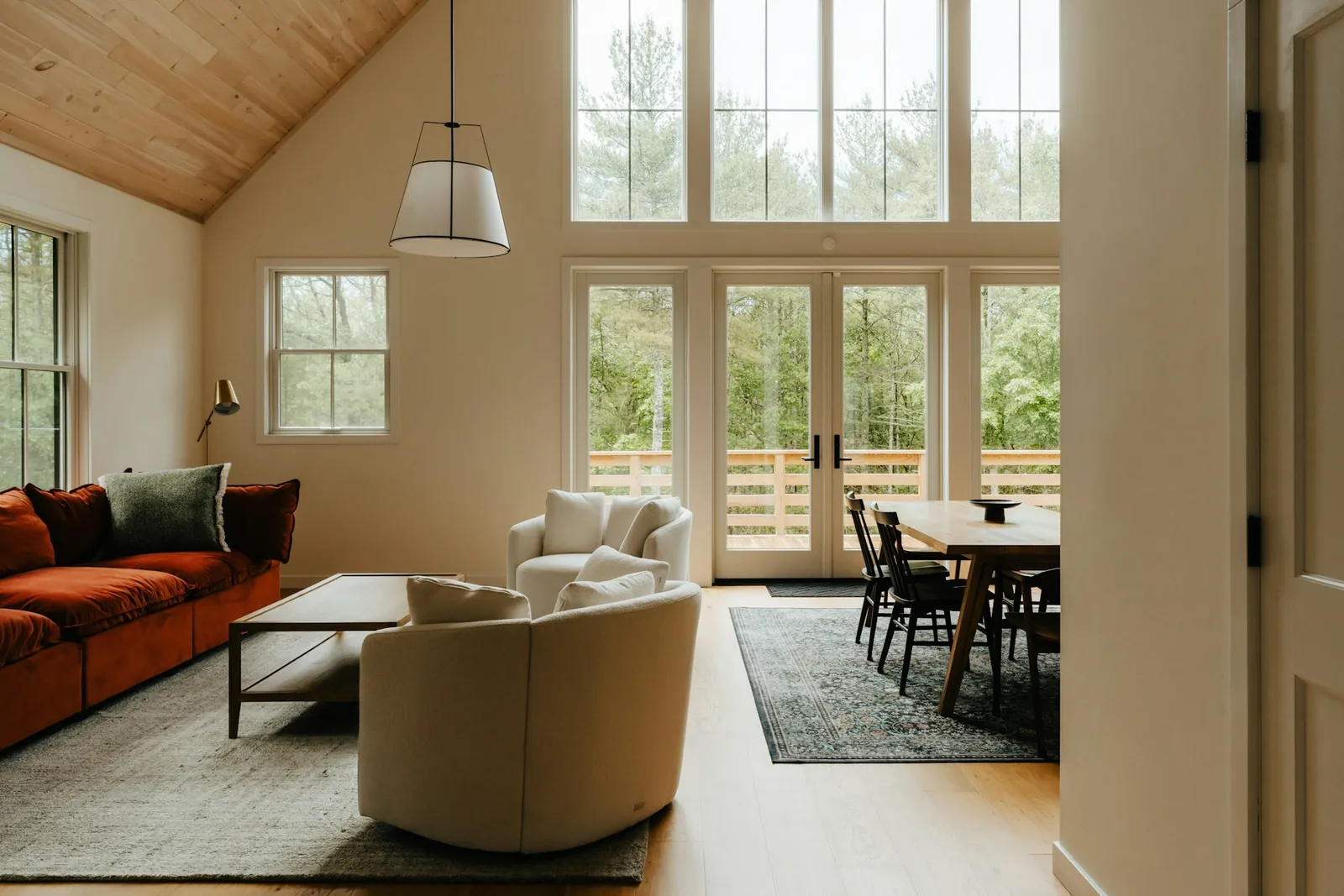 Interior of a contemporary cottage with a cathedral ceiling and large picture windows opening onto the forest